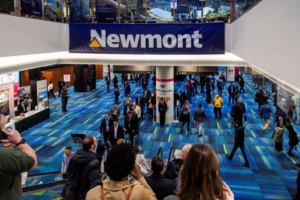 People mill around in a conference floor setting, with a sign reading 'Newmont'.