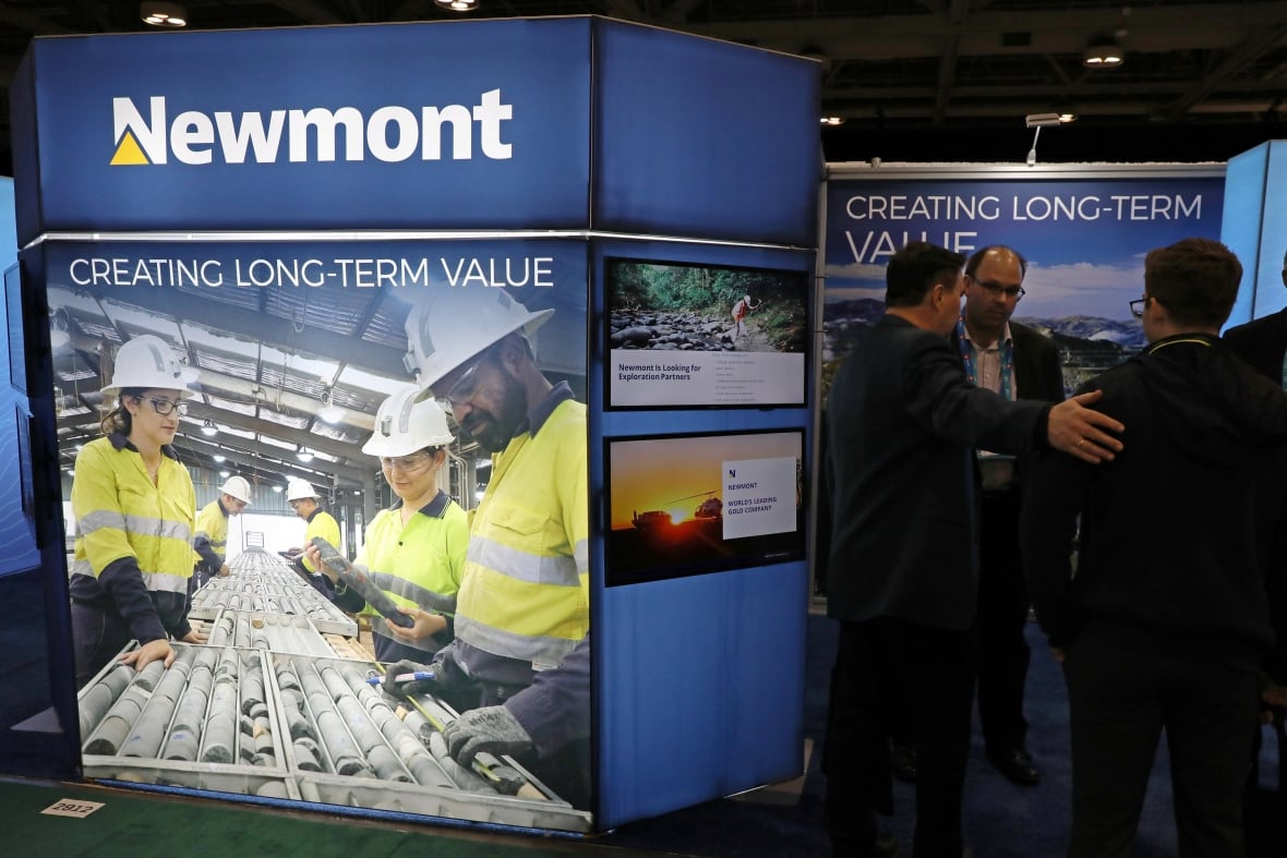 A group of people speak next to a booth marked 'newmont' in a conference setting.