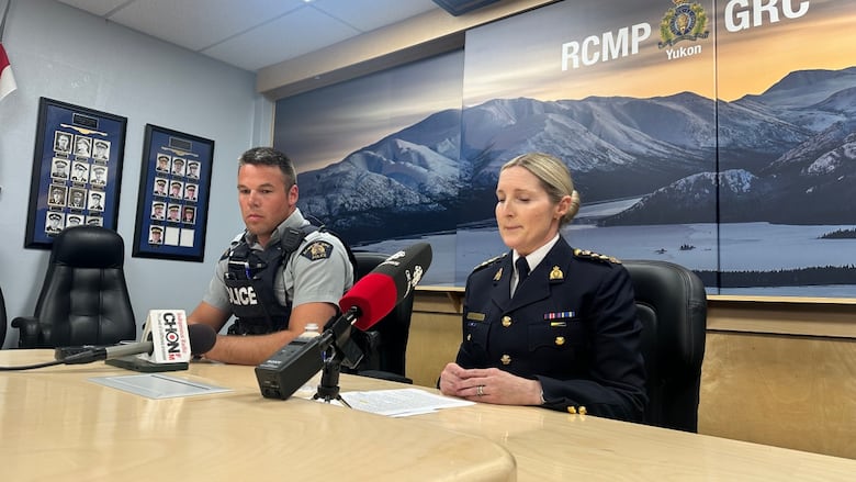 Two RCMP officers sit at a table behind microphones.
