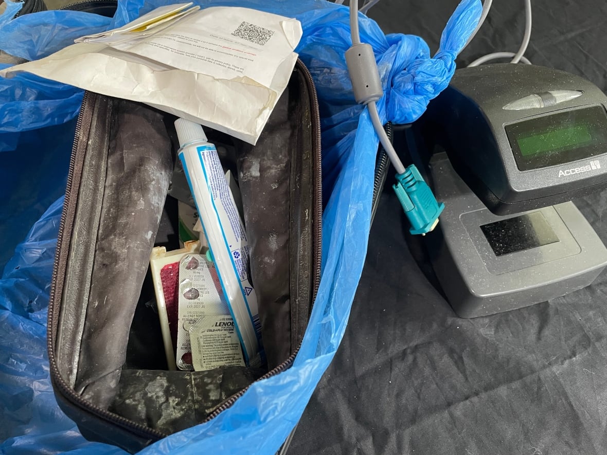 Se abrió una bolsa de inodoro visible para mostrar algunas drogas y tubo de pasta de dientes. Hay una máquina de escaneo de boletos al lado.