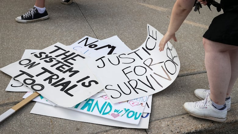 A hand reaches down towards a pile of white signs on a sidewalk.