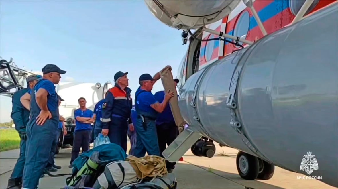 Several men in uniforms and ball caps stand near a small aircraft. Some are loading supplies on to the plane.