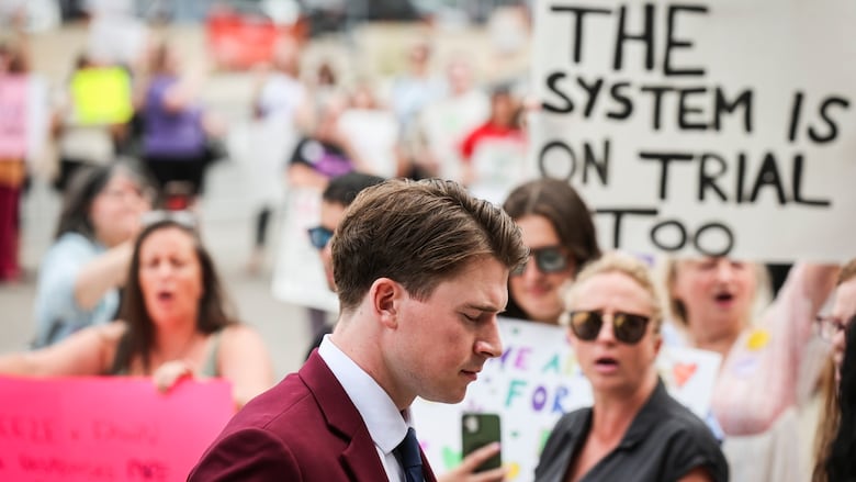 A man in a red suit walks by a group of people holding signs on a sidewalk.
