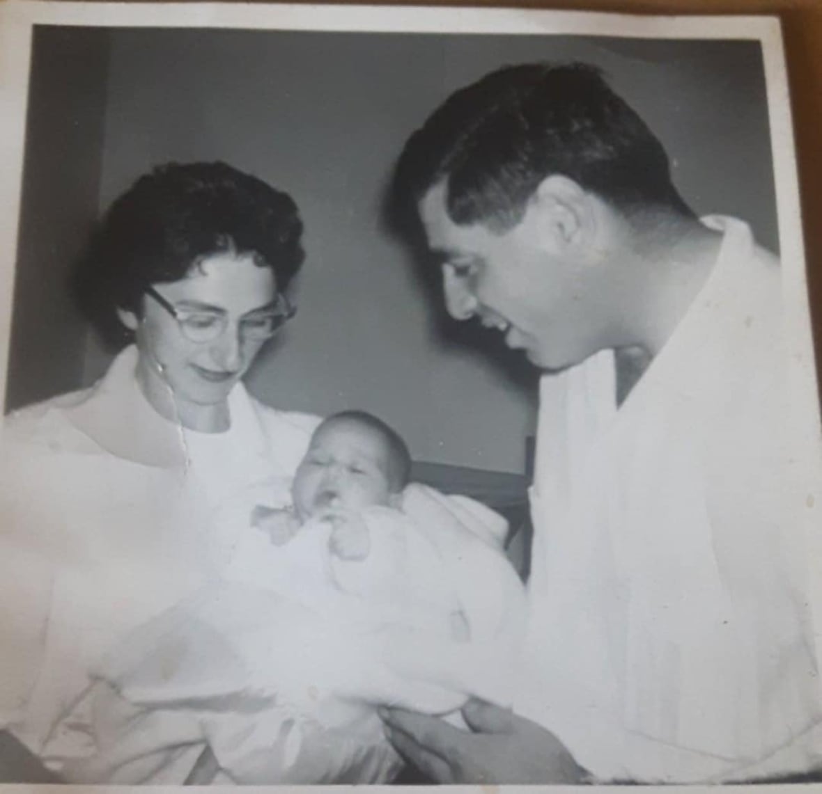 A black and white pictures shows a man and a woman holding a baby wrapped in a blanket.