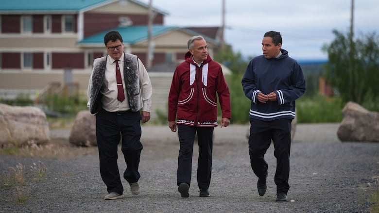 Three men walk along a gravel path.