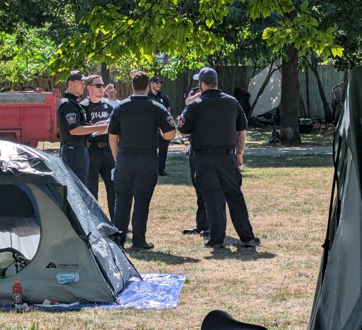Uniformed officers talk to each other at a park, some tents can be seen around them
