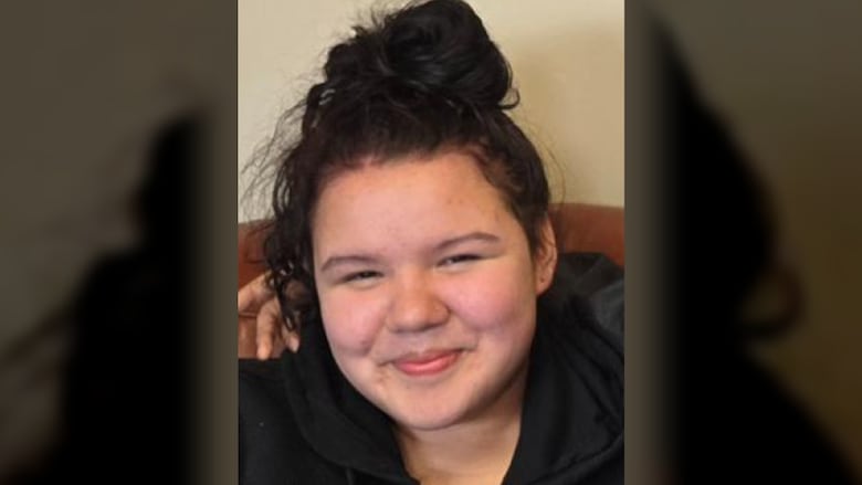 A teen with long hair tied up in a ponytail smiles in a photo.