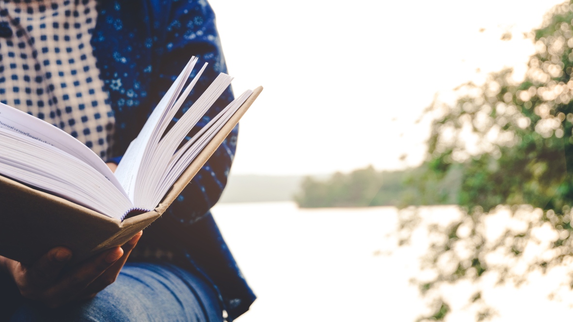 stock image of a person sitting by a lake, reading.