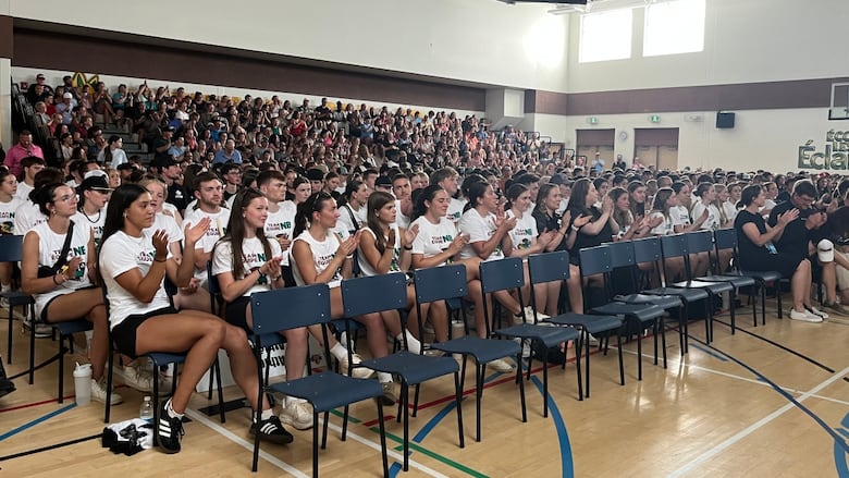 A room full of students sitting in bleachers and clapping