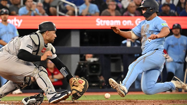 Toronto Blue Jays outfielder Davis Schneider scores a run ahead of a tag by New York Yankees catcher J.C. Escarra in the fifth inning of a July 23, 22025 MLB regular-season game in Toronto.