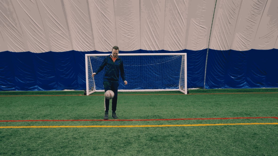 A man kicks a soccer ball in front of a goal.