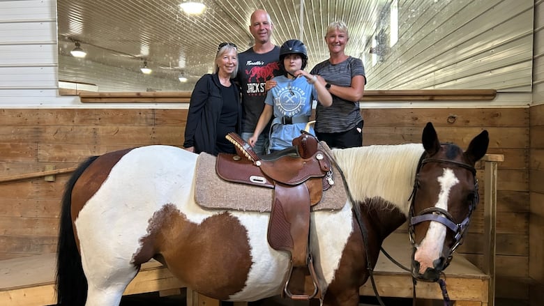 A family of four stands near a horse inside of a barn.