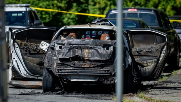 A burnt car is pictured with its door open on a road.