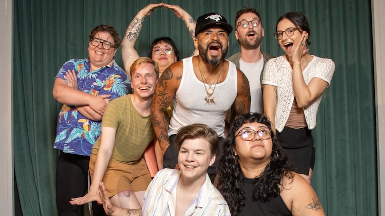 On a short stage with a green curtain, a group of eight people pose.