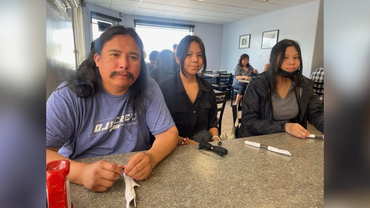 Three people are seen sitting at a table at a restaurant.