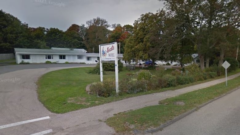 A deserted low-rise motel is shown on a tree-lined street.