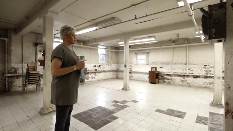 Woman stands in large dilapidated room.