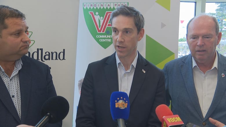 Three men in blue sports jackets stand in front of microphones.