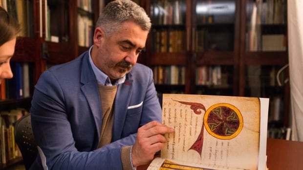 A man wearing a suit turns the page of an old book with ancient writings in a library