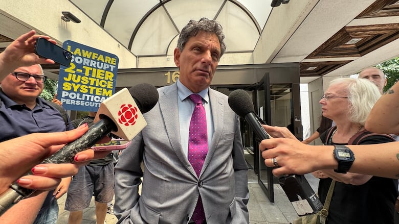 A man in a suit is interviewed by multiple reporters.