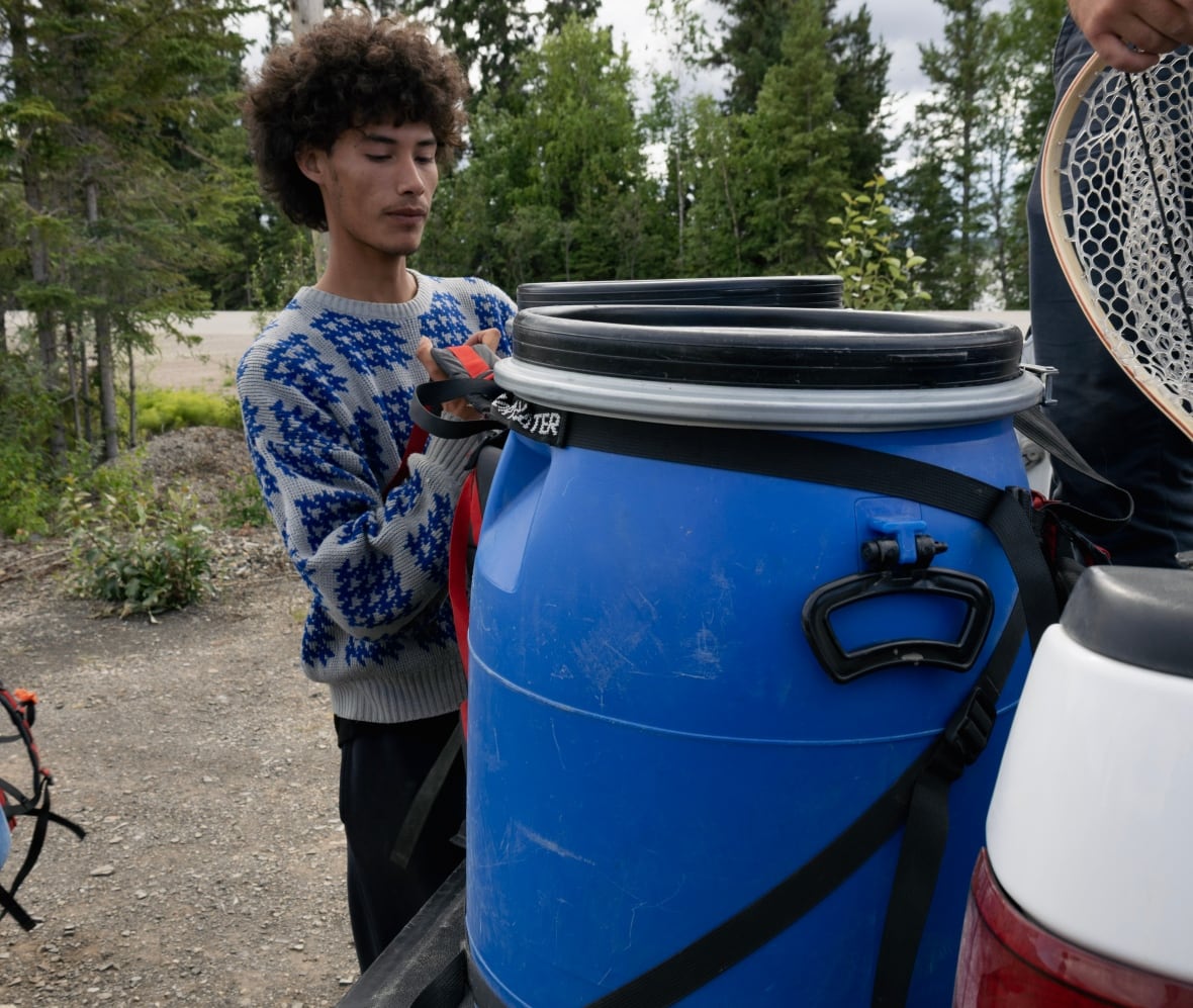 A youth in a sweater picks up a big blue barrel.