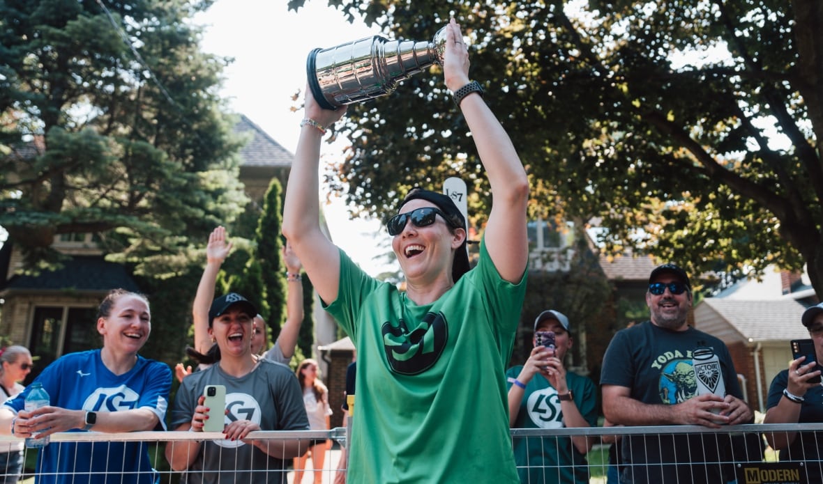 A woman in a green t-shirt holds up a trophy triumphantly.