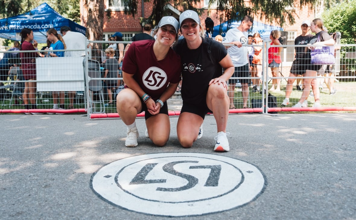Two women pose in front of a circle that says LS7 in front of a crowd.