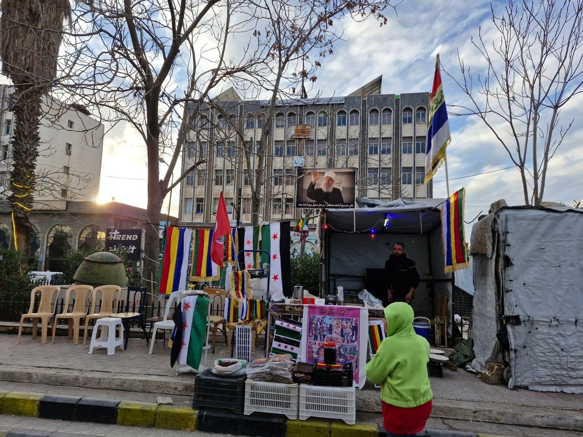 A person in front of the kiosk with flags near a large building.