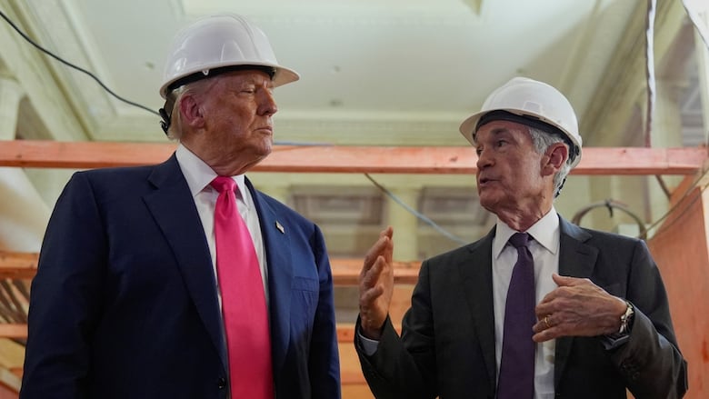 Two men in suits, wearing white construction hard hats, looking at each other while talking