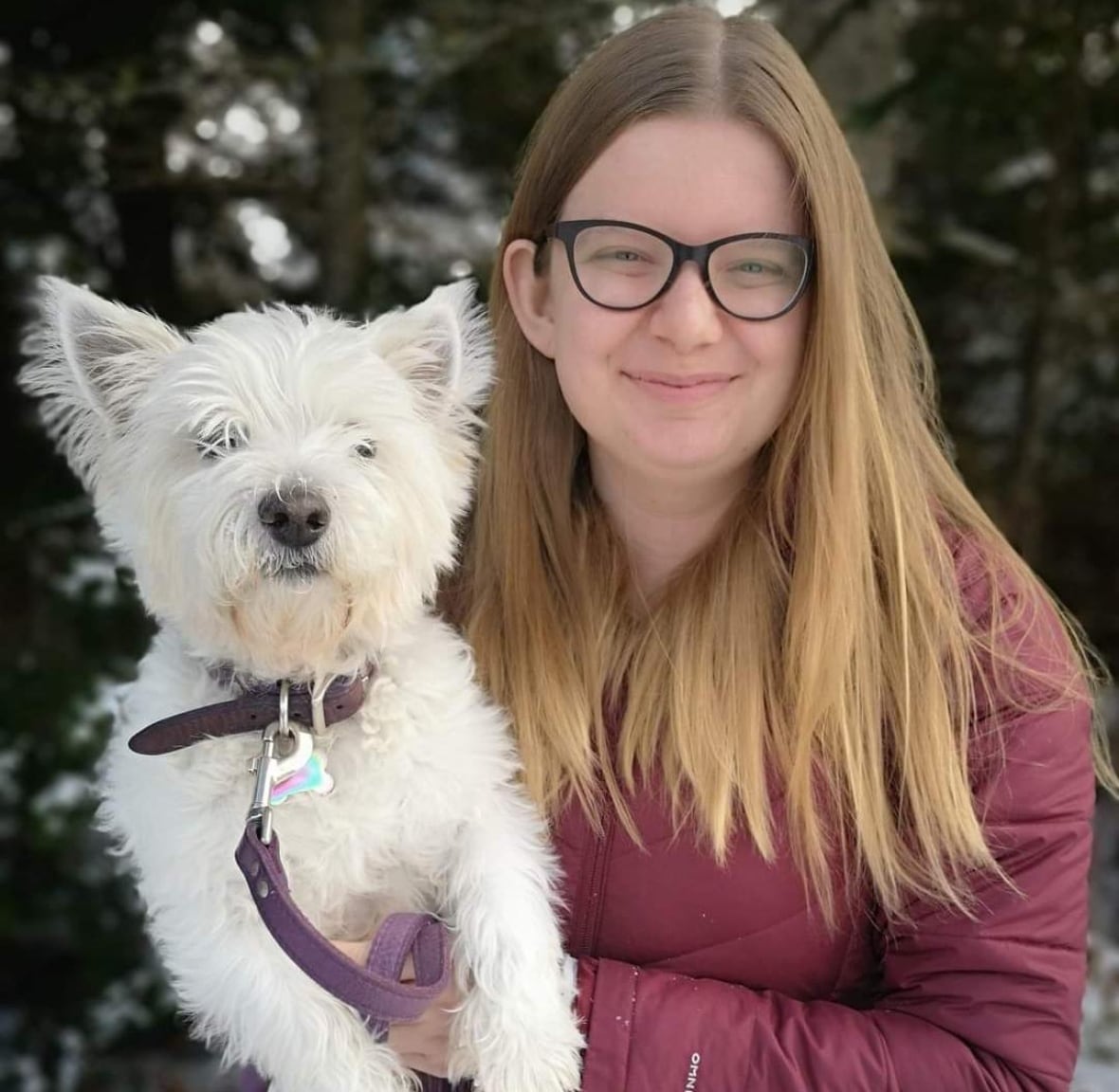 A smiling woman with blond hair poses for a photo with a white dog in her arms.
