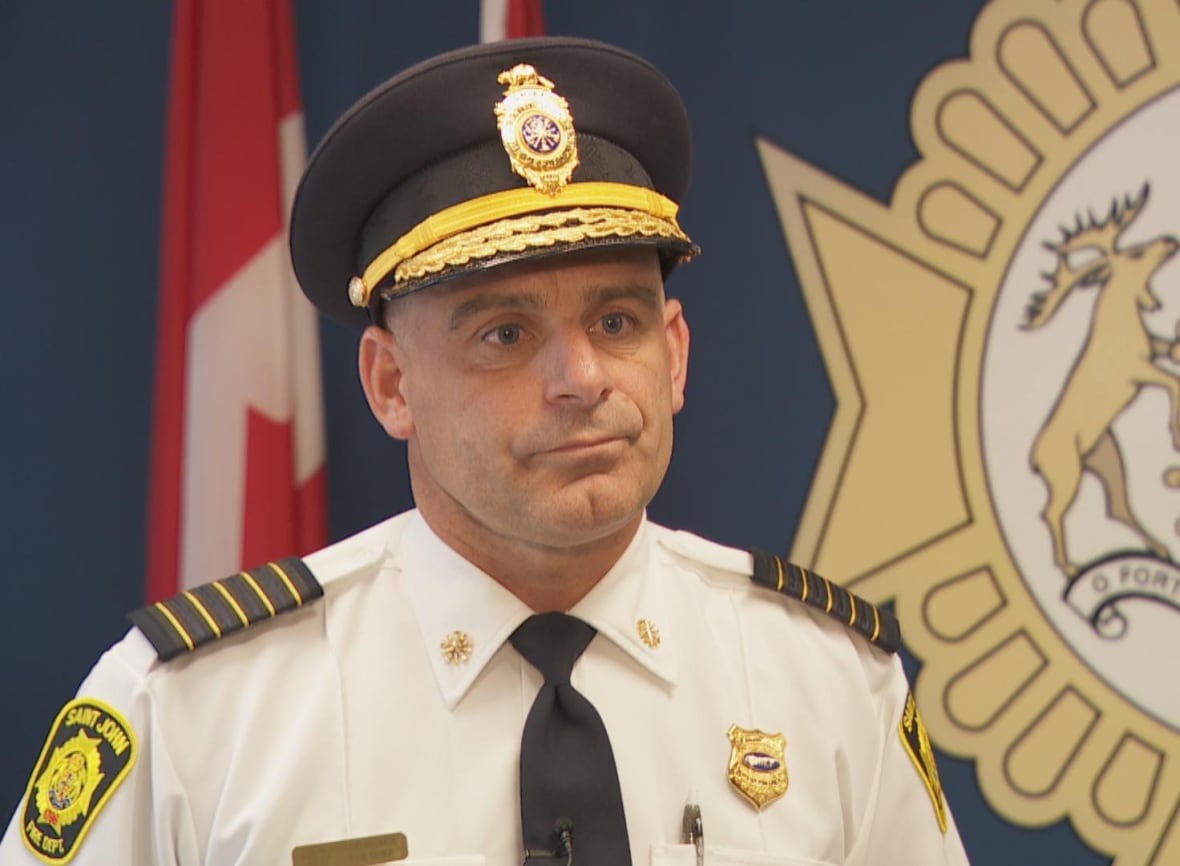 Man looking off side of camera with a neutral expression wearing a fire chief uniform. 