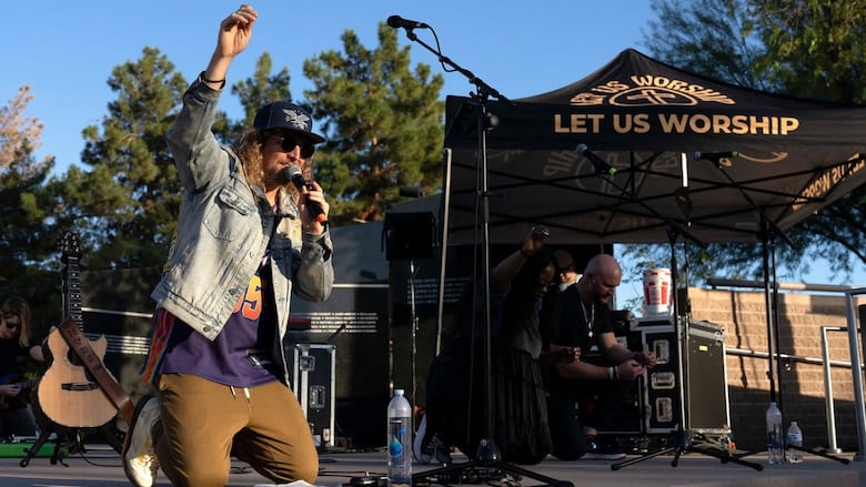 Man in jean jacket on his knees pointing toward sky on stage