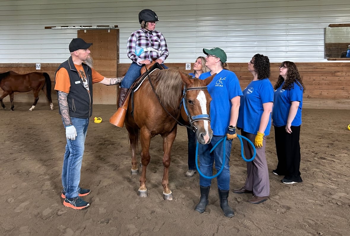 A group of volunteers gather around a horse, and a participant of the Thunder Bay Therapeutic Riding Association.