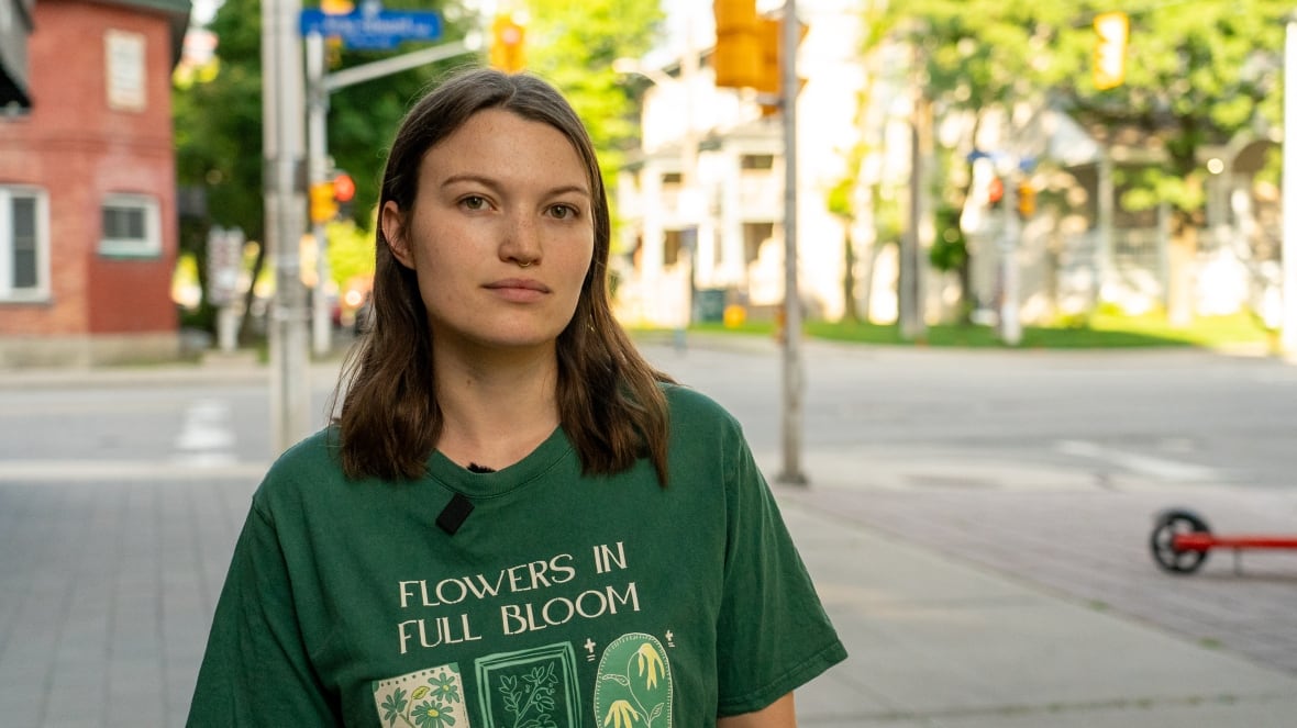 a woman standing outside on a sidewalk with an intersection in the background.