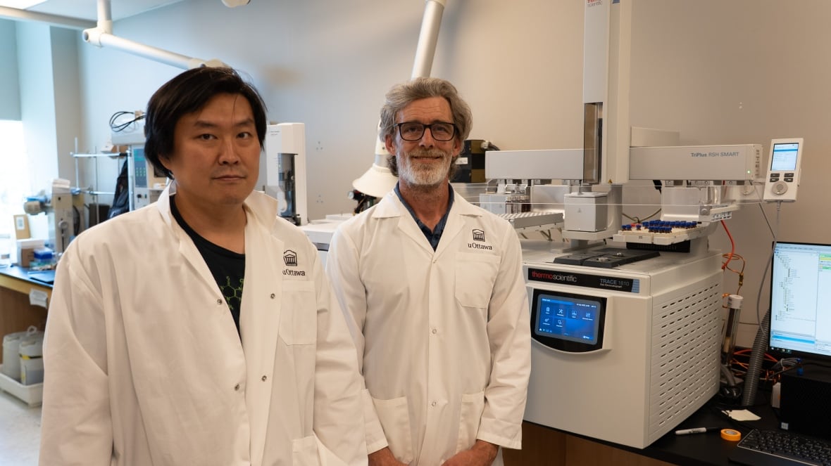 Two men with lab coats stand in front of a machine.