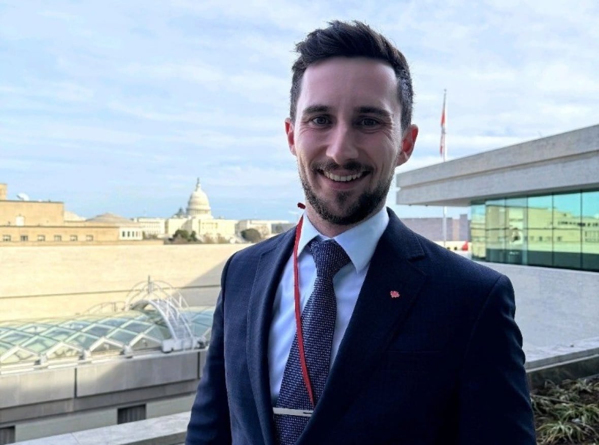 A man in a suit standing outdoors with buildings and a dome in the background