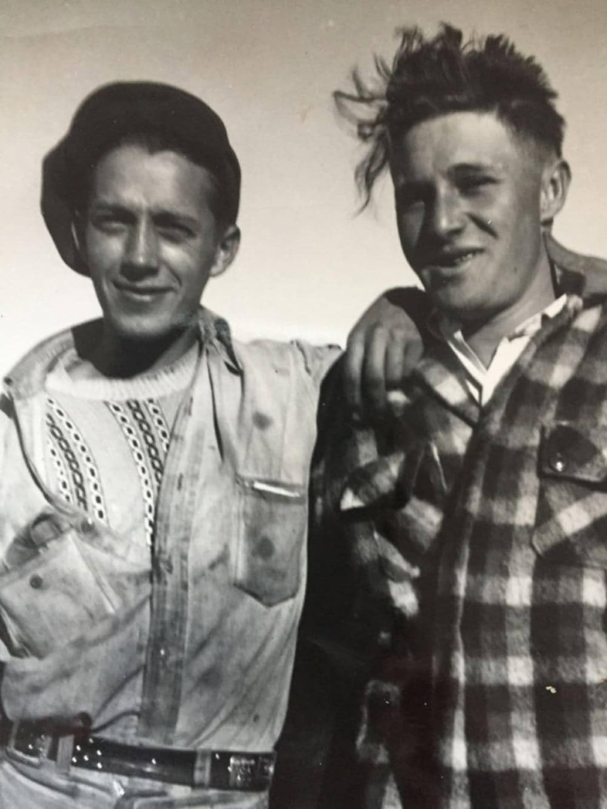 A black and white photos shows two young men, arms around each other.