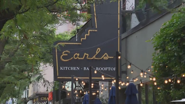 Sign for a restaurant reading, 'Earls, Kitchen, Bar and Rooftop." The sign is outdoors and is black with gold lettering.