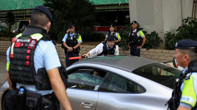 About a half-dozen police officers of Asian descent in uniform are shown surrounding a vehicle.