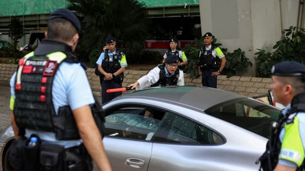 About a half-dozen police officers of Asian descent in uniform are shown surrounding a vehicle.