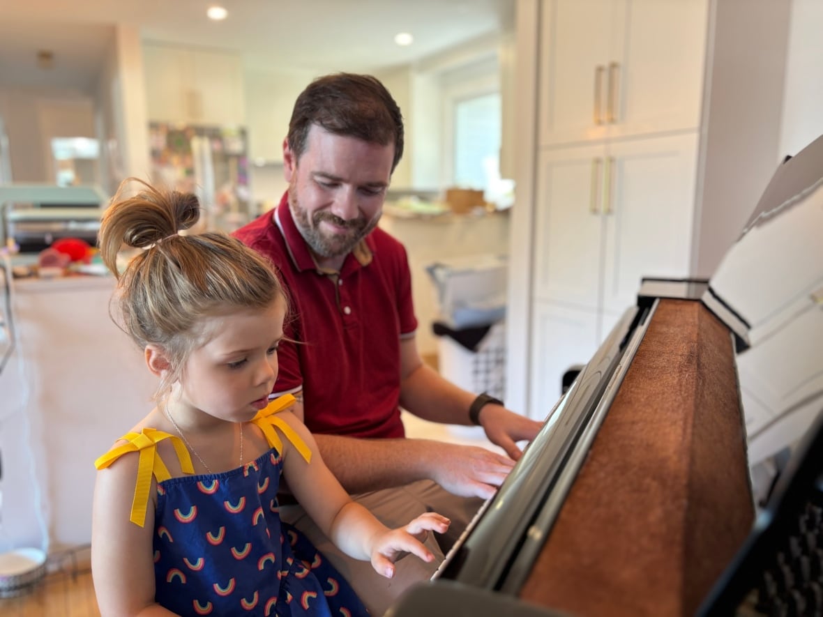 A man and a young girl sit side by side at a piano.