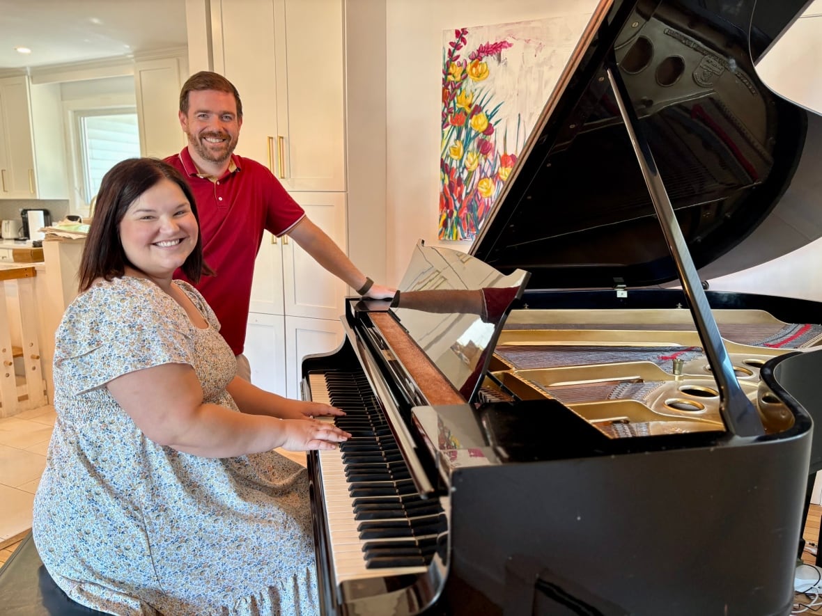 A man standing at a piano and a woman sitting on the bench with her hands on the keys.