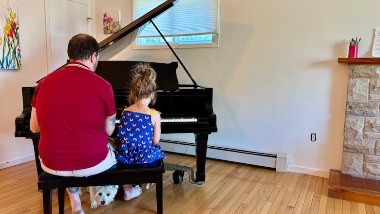 A man and small child sitting at a piano, photographed from behind.