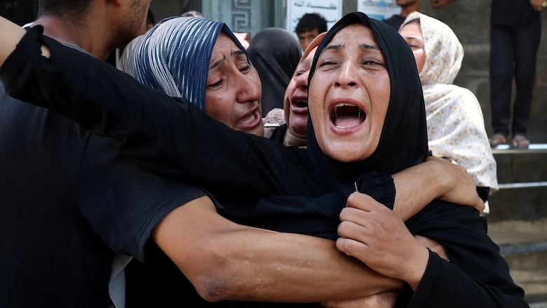 A woman holds another woman as she yells out in agony at a funeral.