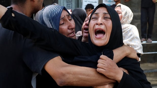 A woman holds another woman as she yells out in agony at a funeral.