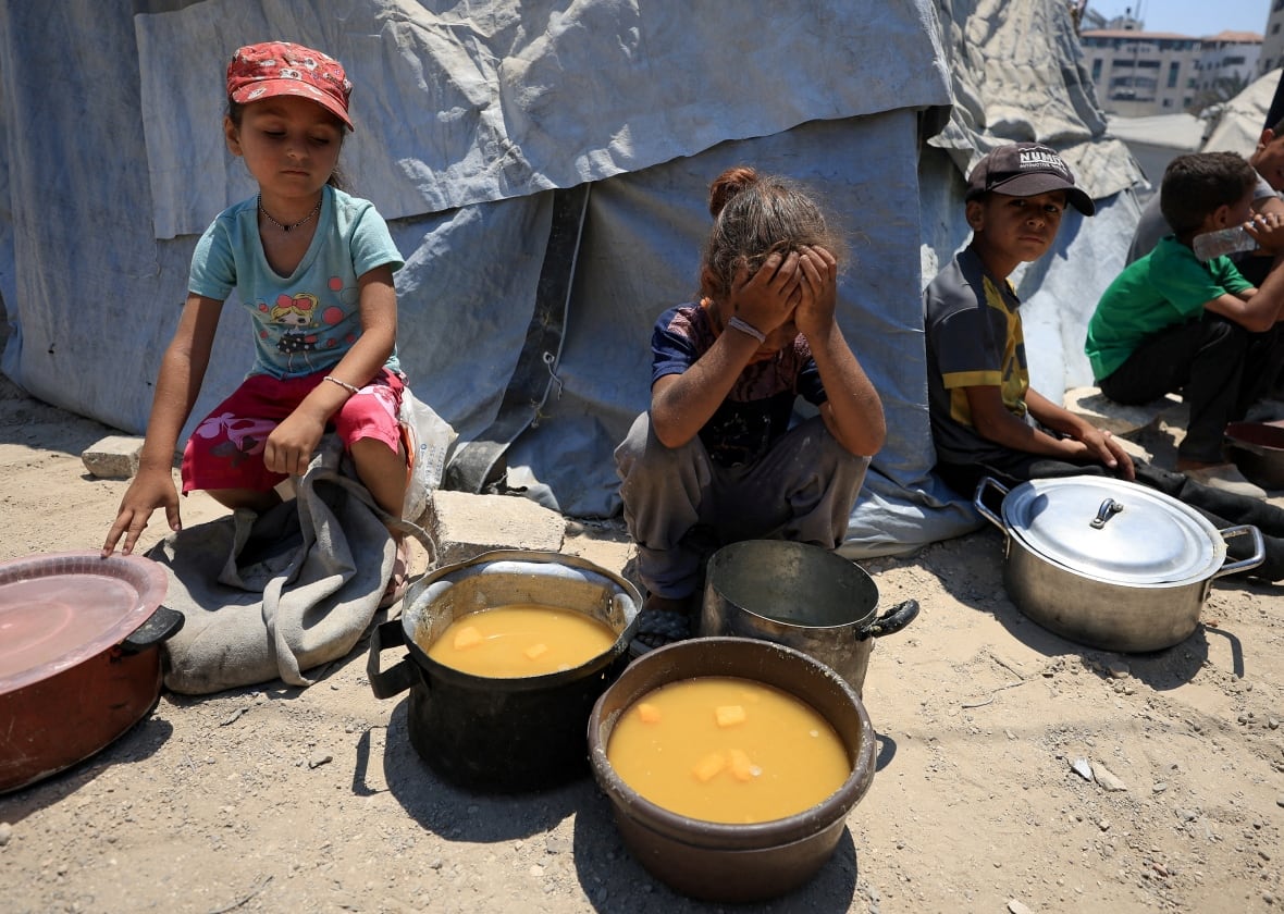 Children sit down near food pots.