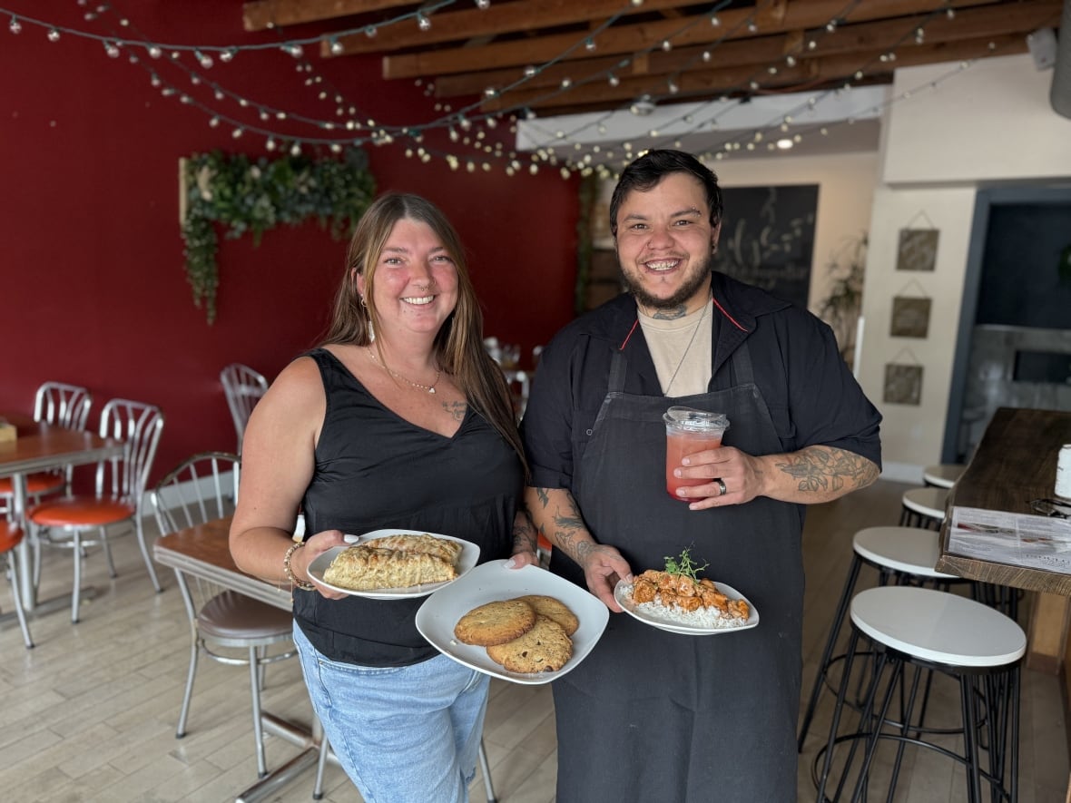 A woman and man stand in a restaurant, holding plates and a drink. 