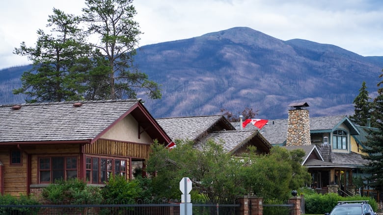 Three two-storey homes with cedar-shingled roofs sit in the foreground of a mountain backdrop in the Jasper townsite. 