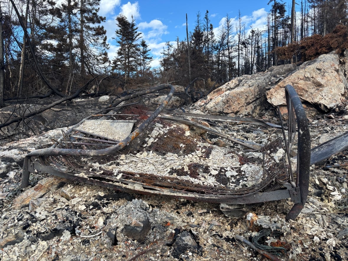 A twisted metal bedframe sits among a pile of ash and debris.