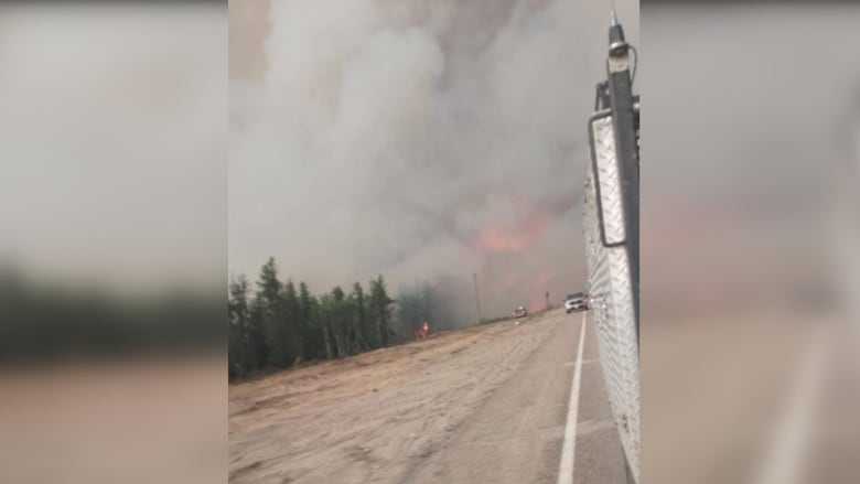 Smoke and fire are seen in the background, along a highway